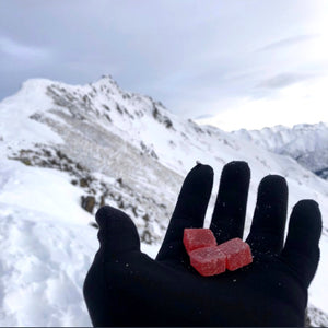Person’s gloved hand holding 3 Red Raven CBD gummies against the background of an Anchorage, Alaska mountain range