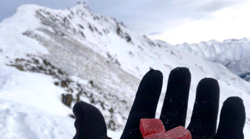 Person’s gloved hand holding 3 Red Raven CBD gummies against the background of an Anchorage, Alaska mountain range